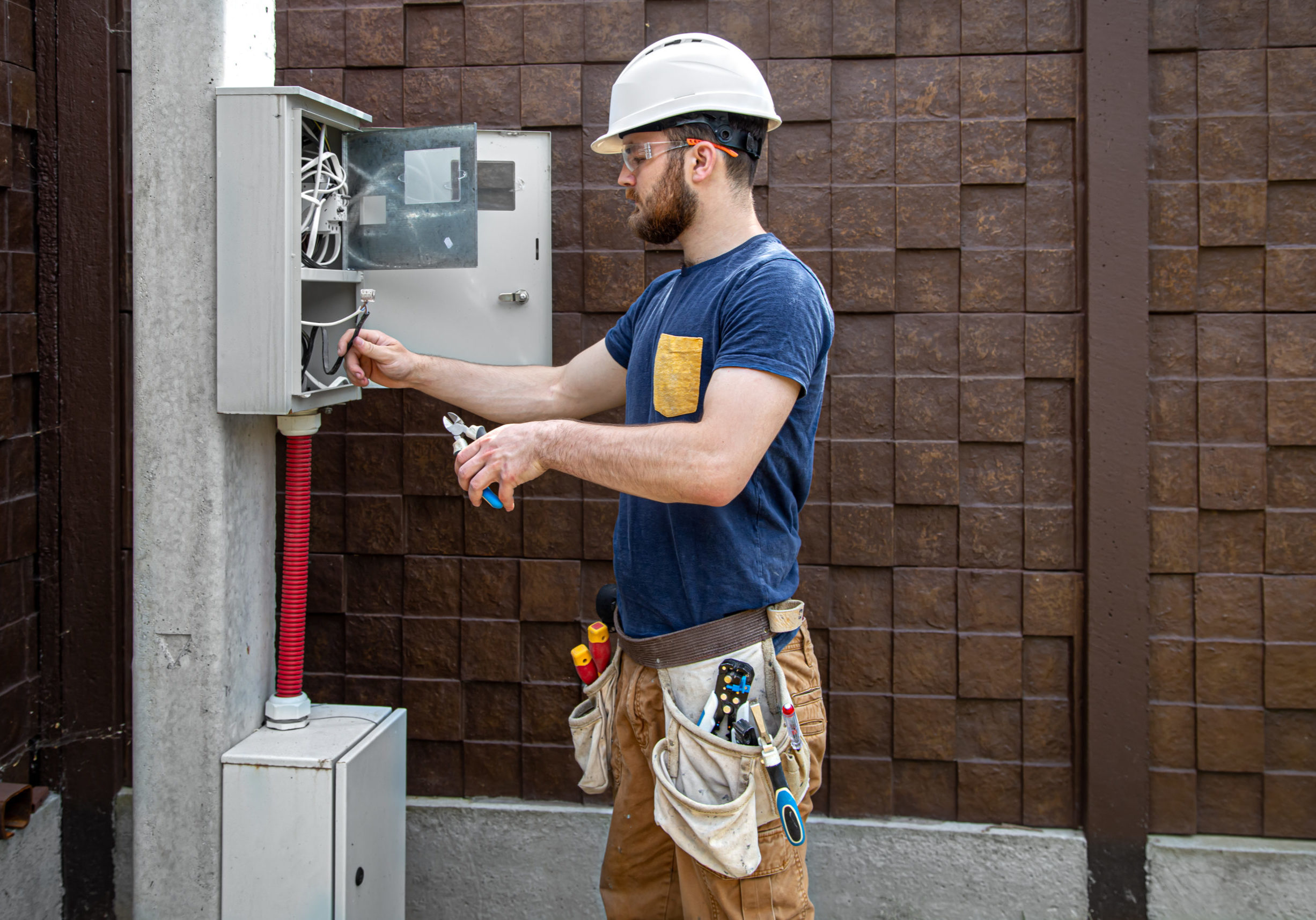 Electrician Builder at work, examines the cable connection in the electrical line in the fuselage of an industrial switchboard. Professional in overalls with an electrician's tool. The concept of working as a professional.