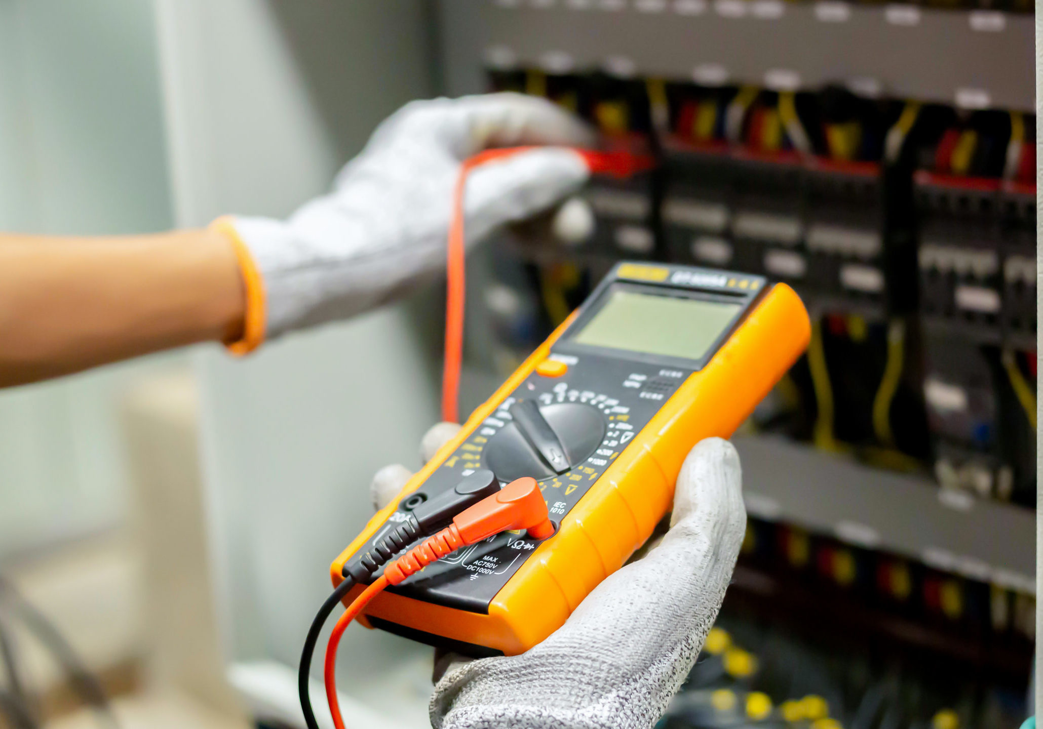 Electrician engineer uses a multimeter to test the electrical installation and power line current in an electrical system control cabinet.