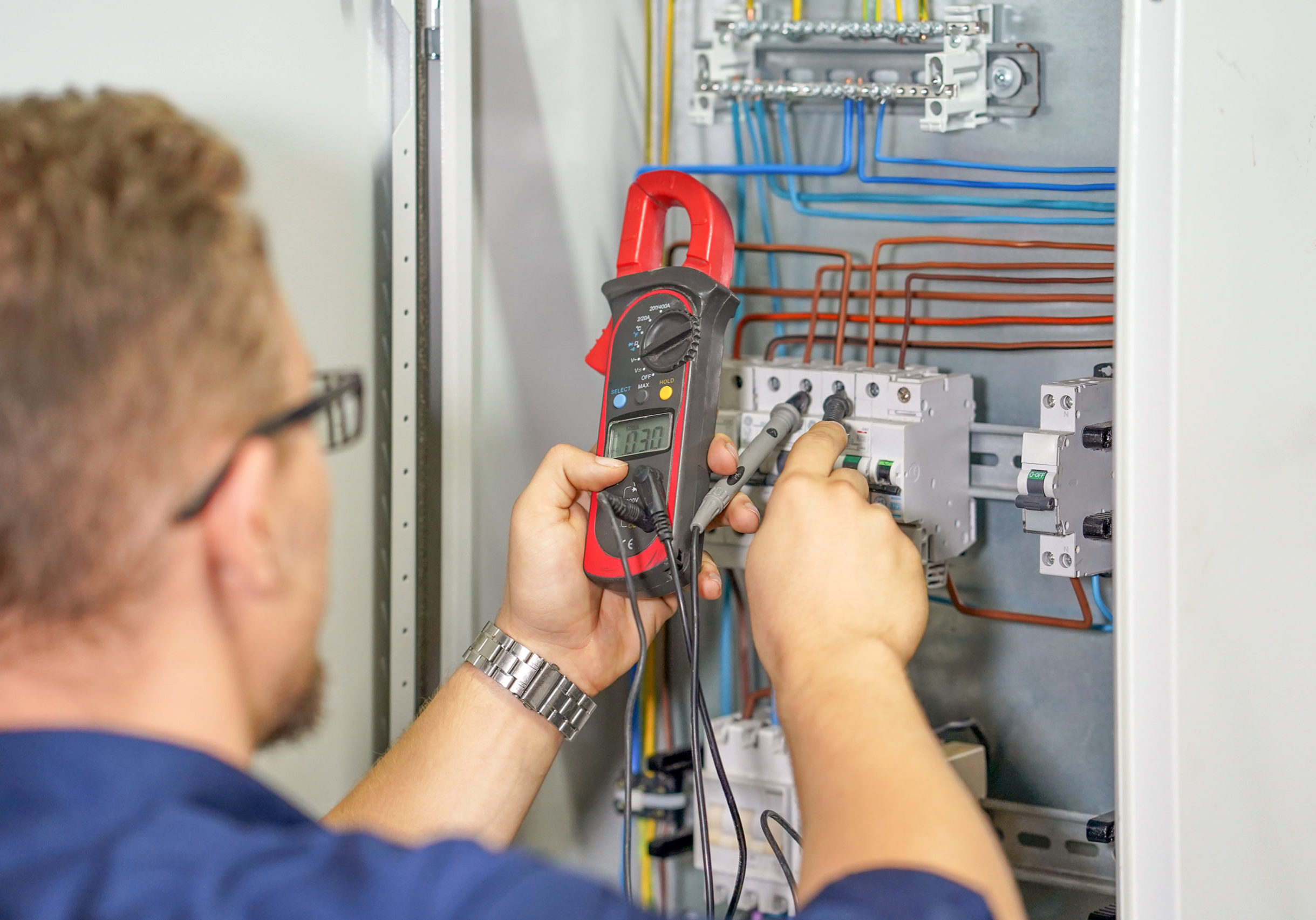 Electrician man measures voltage with multimeter in electrical cabinet. An electrician is checking the voltage in an electric box. Adjustment of electrical control circuit for industrial equipment. Toning